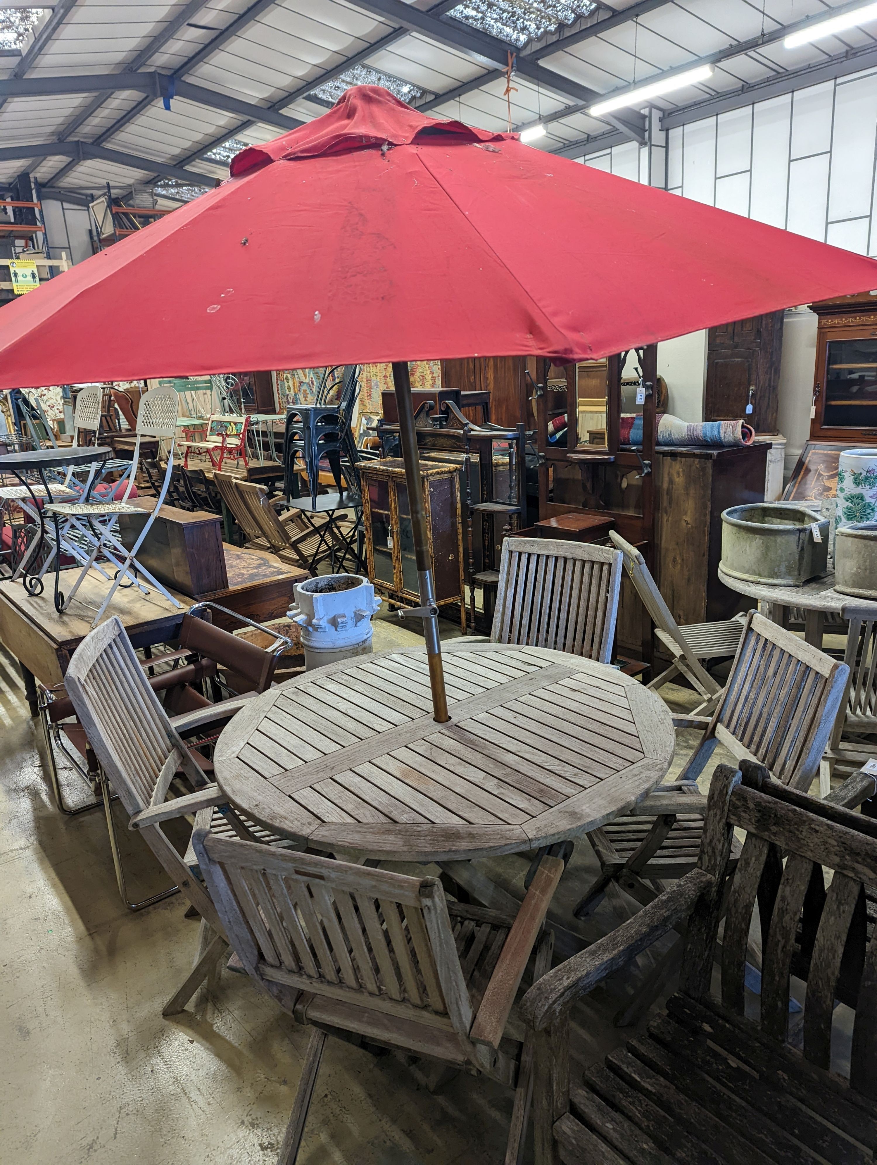A circular weathered teak folding garden table, diameter 120cm, height 74cm, four folding elbow chairs and a parasol